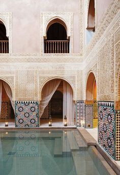 an indoor swimming pool in the middle of a building with arches and pillars on either side