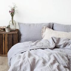 an unmade bed with blue linens and pillows on the side table next to it