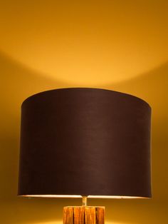 a table lamp with a wooden base and black shade on the top, against a yellow wall