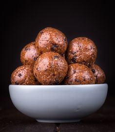 a white bowl filled with chocolate covered donuts on top of a wooden table next to a black background