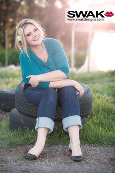 a woman sitting on top of a tire in the grass with her arms crossed and smiling