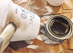 a paint can with a brush next to it on top of some brown and white paper