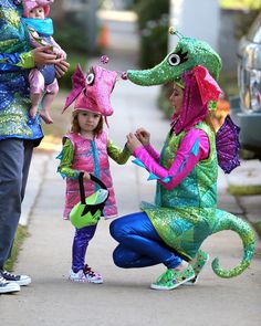 three children dressed in costumes standing on the sidewalk with an adult and child holding hands