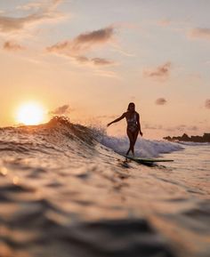 a woman riding a surfboard on top of a wave in the ocean at sunset