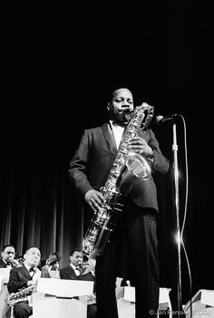 a man standing in front of a microphone while holding a saxophone