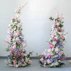 two tall floral arrangements sitting next to each other on top of a gray floor covered in white and pink flowers