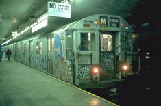 a subway train with graffiti on the side and people walking near by at night time