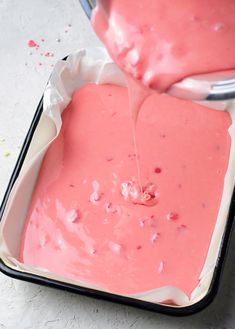 someone is pouring something into a pan with pink icing on it and sprinkles all over the top