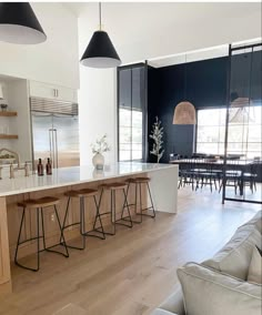 an open kitchen and living room area with bar stools in the foreground, dining table on the far side