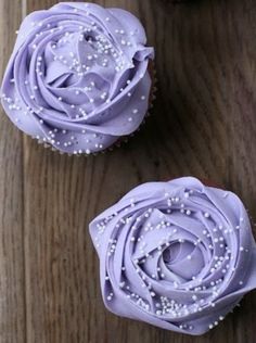 two cupcakes with purple frosting and sprinkles sitting on a wooden table