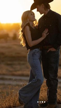 a man and woman standing next to each other in a field with the sun setting behind them