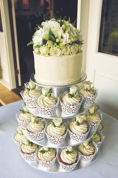 a tiered cake with cupcakes and flowers on the top is sitting on a table