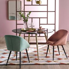 a dining room table with chairs and a vase on it in front of a pink wall