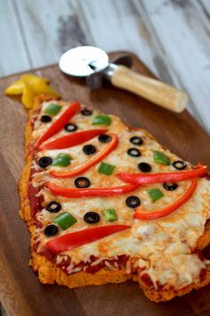 a piece of pizza on a cutting board with olives, peppers and pepperoni