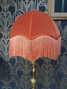 an orange lamp with fringes on it in front of a wallpapered background