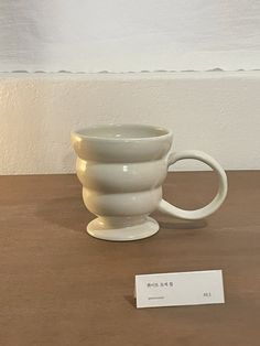 a white coffee cup sitting on top of a wooden table next to a price tag