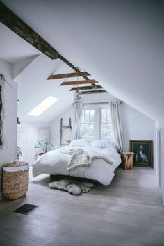 an attic bedroom with white bedding and wooden beams on the ceiling is decorated in natural materials