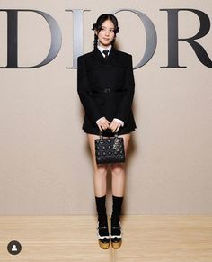 a woman standing in front of a dior sign holding a black purse and looking at the camera