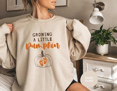 Growing A Little Pumpkin Sweatshirt, Maternity Crew Neck Sweatshirt, Pregnancy Reveal Hoodie, Halloween Pregnancy Announcement, Pumpkins Celebrate the joy of pregnancy in style with our "Growing A Little Pumpkin" Maternity Crew Neck Sweatshirt. This cozy and comfortable sweatshirt is the perfect way to make your fall pregnancy announcement or reveal the exciting news to family and friends. Crafted with soft, high-quality materials, it ensures comfort throughout your journey. Its adorable pumpkin-themed design not only captures the essence of autumn but also adds a touch of charm to your maternity wardrobe. With a relaxed fit and room to accommodate your growing baby bump, this sweatshirt is a must-have for any expectant mother. Whether you wear it casually or for a special announcement, it Thanksgiving Pregnancy Announcement, Fall Pregnancy, Halloween Gender Reveal, Fall Pregnancy Announcement, Halloween Pregnancy Announcement, Thanksgiving Sweater, Gender Reveal Gifts, Maternity Ideas, Thanksgiving Sweatshirt