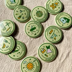 six green badges with different symbols on them sitting on a bed sheet in front of a white towel