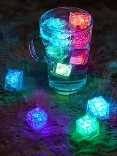 glowing ice cubes in a glass mug on fuzzy carpeted area with green and purple lights