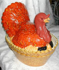 a ceramic chicken sitting in a basket on a white cloth covered tablecloth with other items