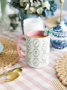 a pink and white checkered table cloth with a cup of tea on it next to gold utensils