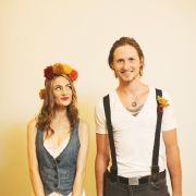 a man and woman standing next to each other wearing flower crowns on their heads, in front of a yellow wall