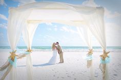 a bride and groom standing under an arch on the beach