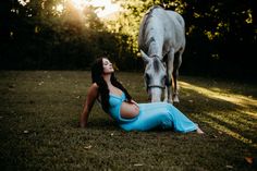 a pregnant woman laying on the ground next to a horse