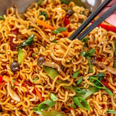 a bowl filled with noodles, vegetables and chopsticks