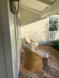 two wicker chairs sitting on a brick patio next to a white wall and window