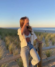 a woman leaning on a fence at the beach