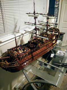 a model pirate ship on display in a room with white shutters and glass table