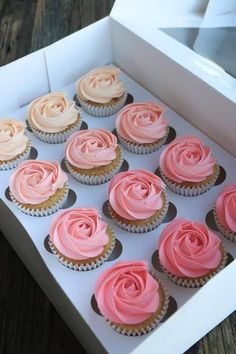 twelve cupcakes with pink frosting in a white box on a wooden table