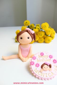 a birthday cake with a girl figurine next to it and flowers in the background