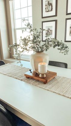 a table with a vase and candle on it in front of pictures hanging on the wall