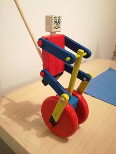 a wooden toy on top of a table next to a blue and red object with a stick sticking out of it