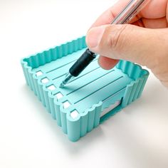 a hand holding a pen and writing on a piece of blue plastic with holes in it