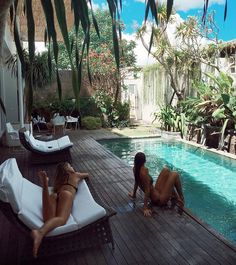 two women lounging on lounge chairs next to a swimming pool in a tropical setting