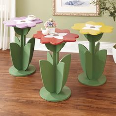 three colorful flower shaped tables sitting on top of a hard wood floor next to a potted plant