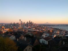 the city skyline is lit up at sunset with mountains in the background and houses on the foreground