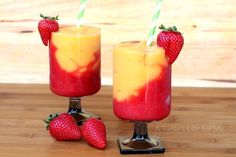 two glasses with strawberries on the rims and one filled with liquid, sitting on a wooden table