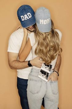 a man and woman hugging each other with hats on their heads, one wearing a hat that says dad