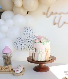 a white cake sitting on top of a wooden stand next to balloons and confetti