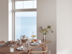 a wooden table with plates and cups on it in front of a window overlooking the ocean