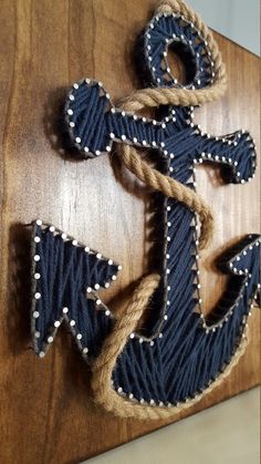 an anchor is made out of rope on a wooden board with white beads and black thread