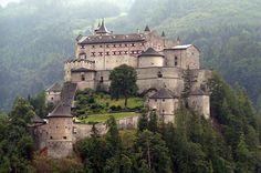 an old castle sitting on top of a hill surrounded by trees and hills in the background