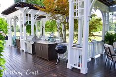 an outdoor kitchen and grill area on a wooden deck with chairs, table and trees in the background