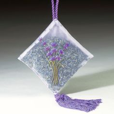 a glass ornament with purple flowers and tassels hanging from a cord